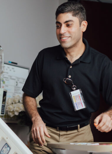 Young male healthcare worker in black polo shirt smiling while working at desk
