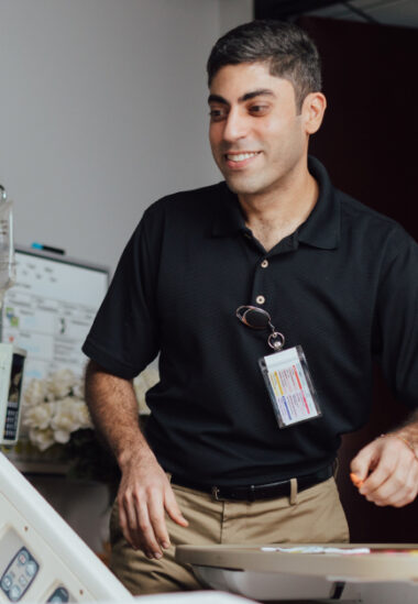 Young male healthcare worker in black polo shirt smiling while working at desk