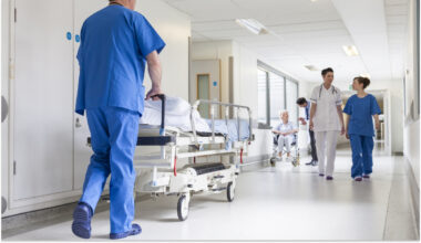 Hospital staff transporting patients and walking down a clean, well-lit corridor in a medical facility.