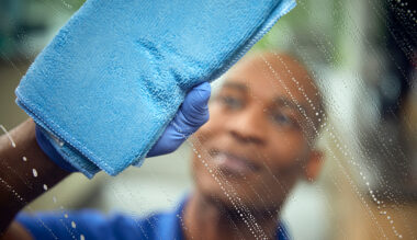 Alt text: Gloved hand wiping glass, leaving a streak-free shine, representing Crothall's cleaning services.