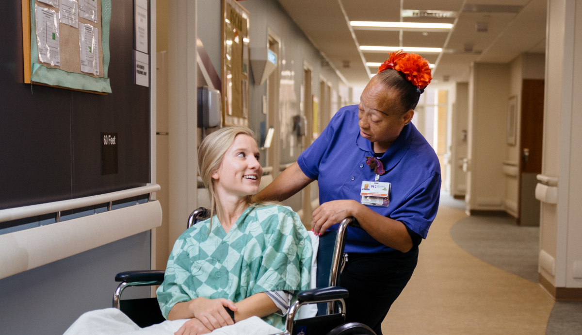 Patient transported in wheelchair by caring hospital staff member in clinic hallway