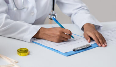 Doctor writing on medical chart with blue pen and stethoscope on table