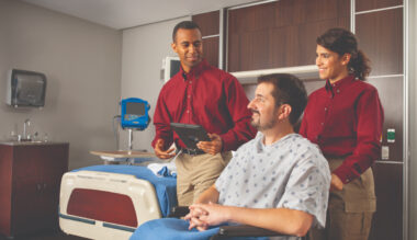 Alt text: Healthcare support staff with patient in hospital room, providing friendly bedside care