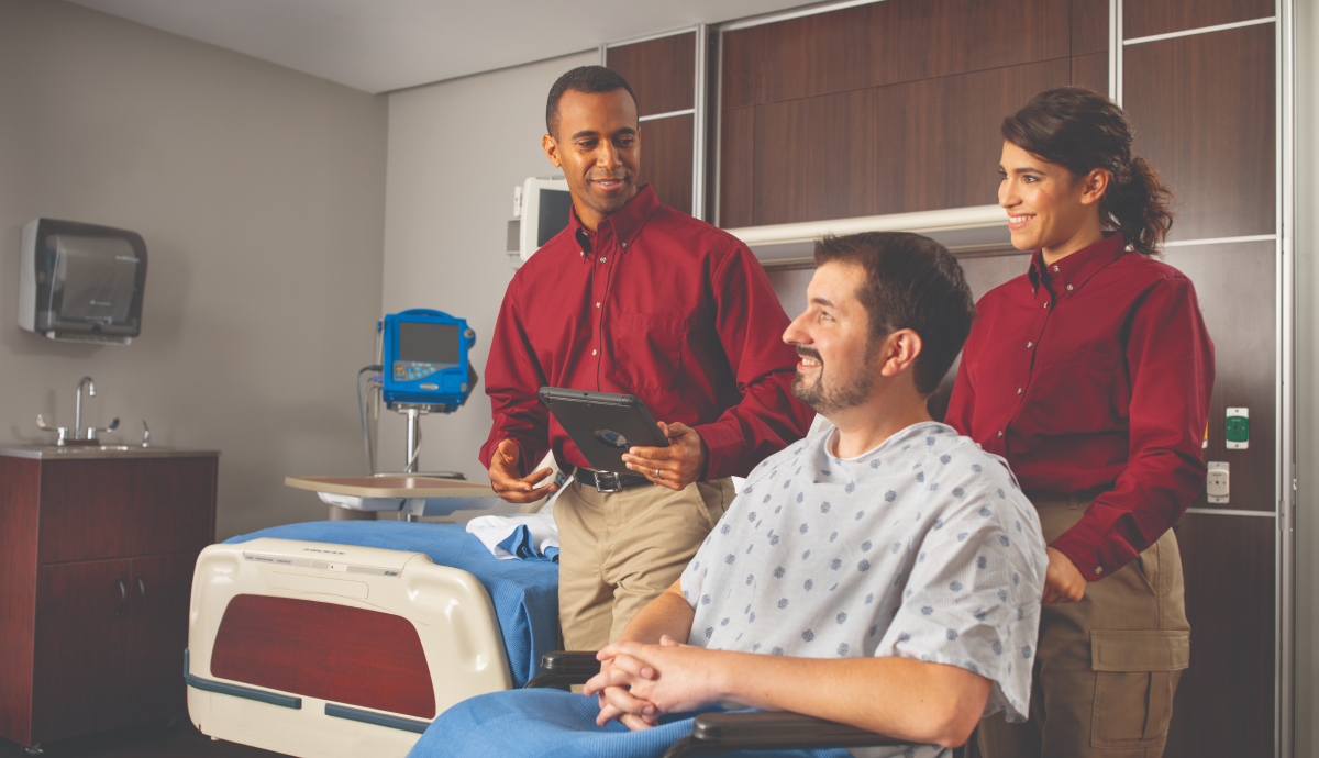 Alt text: Healthcare support staff with patient in hospital room, providing friendly bedside care