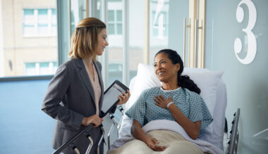 Patient and healthcare worker discuss care plan in hospital room, both smiling