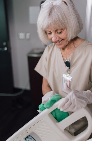 Elderly healthcare worker in scrubs smiles while preparing medication with gloved hands