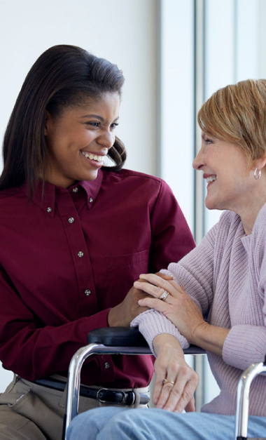 Smiling healthcare worker comforting elderly woman in wheelchair by window