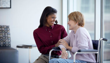 Two women in an office talking and smiling, one in a wheelchair and one standing beside her