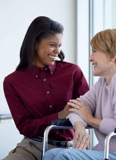 Two women in an office talking and smiling, one in a wheelchair and one standing beside her