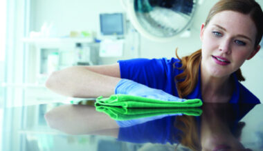 Smiling healthcare worker holding stack of green folded hospital linens in medical facility room