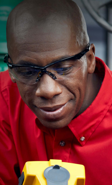 Technician in red shirt and safety glasses examining medical equipment, providing healthcare support services.
