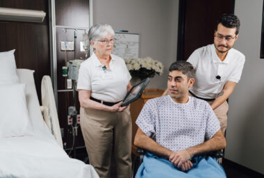 Elderly patient and healthcare workers reviewing medical records in a hospital room