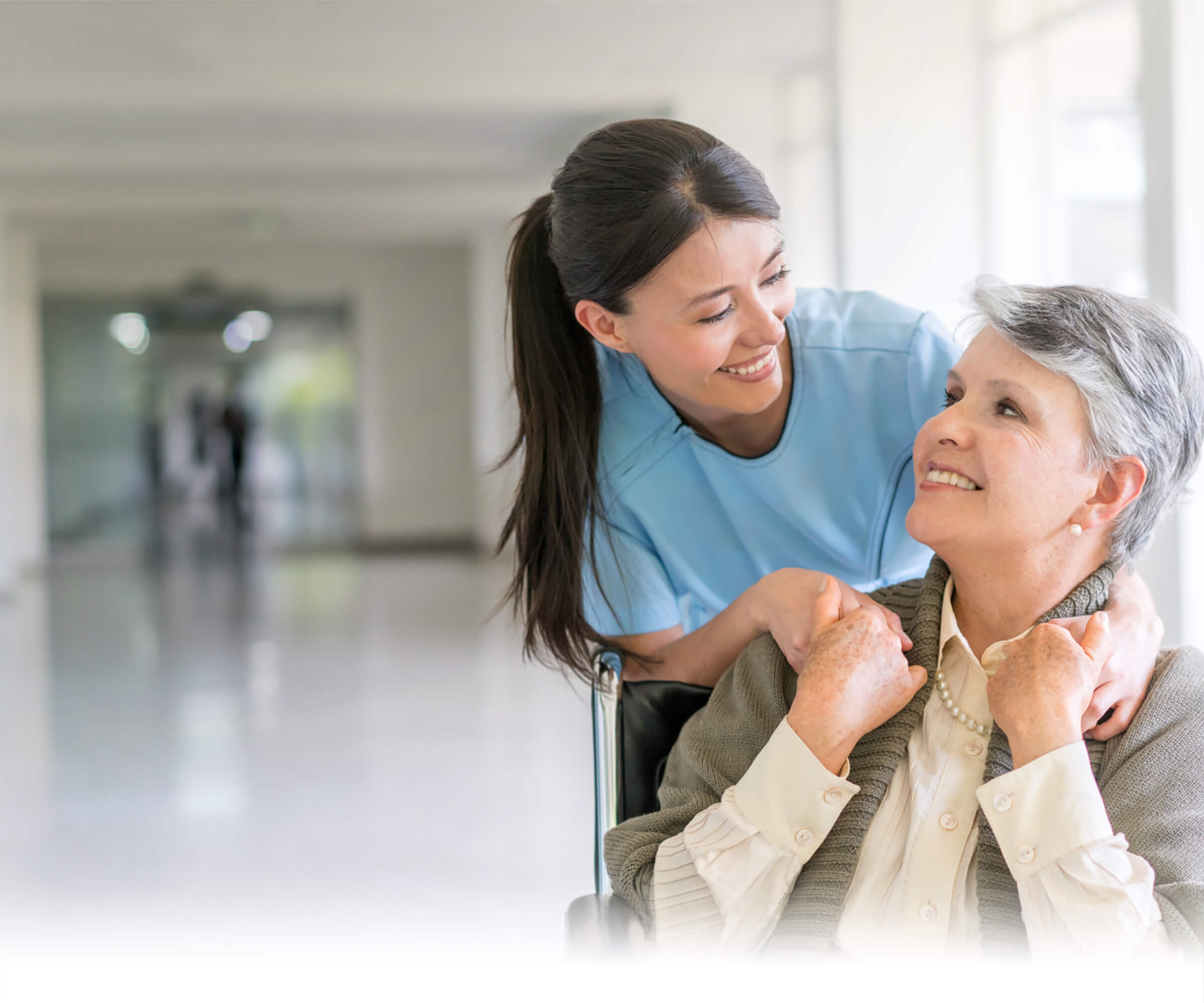 Young healthcare worker lovingly assists smiling elderly woman in wheelchair in bright, modern facility