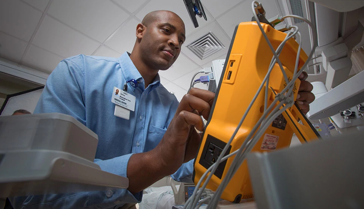 Alt text: Hospital worker in blue shirt inspecting medical equipment in patient room