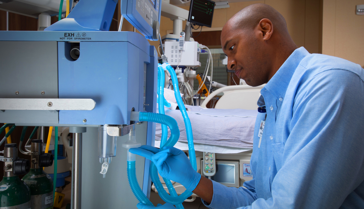 Man in blue scrubs operates medical equipment in hospital room setting