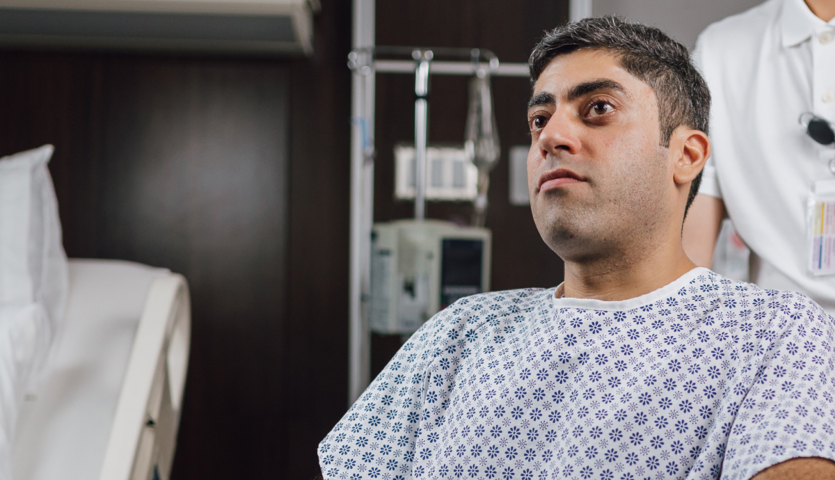 Pensive male patient in hospital gown sitting on bed in dimly lit hospital room