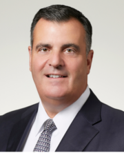 Smiling businessman in suit and tie posing for professional headshot against light background.