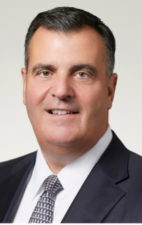 Smiling businessman in suit and tie posing for professional headshot against light background.