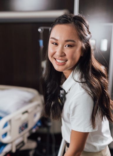 Smiling Asian student in school uniform standing in hallway, looking at camera.