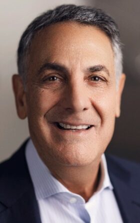 Smiling mature businessman in suit against blurred background, exuding confidence and approachability.
