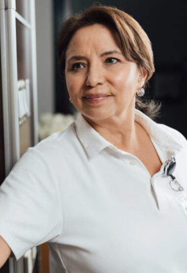 Smiling healthcare professional wearing white uniform shirt looks confidently at the camera.