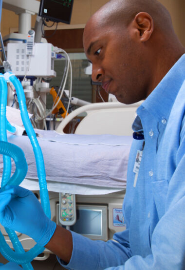 Hospital worker in blue shirt checking medical equipment in patient room