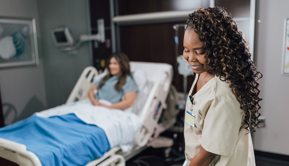 Smiling healthcare worker beside patient's hospital bed, providing compassionate care and support.