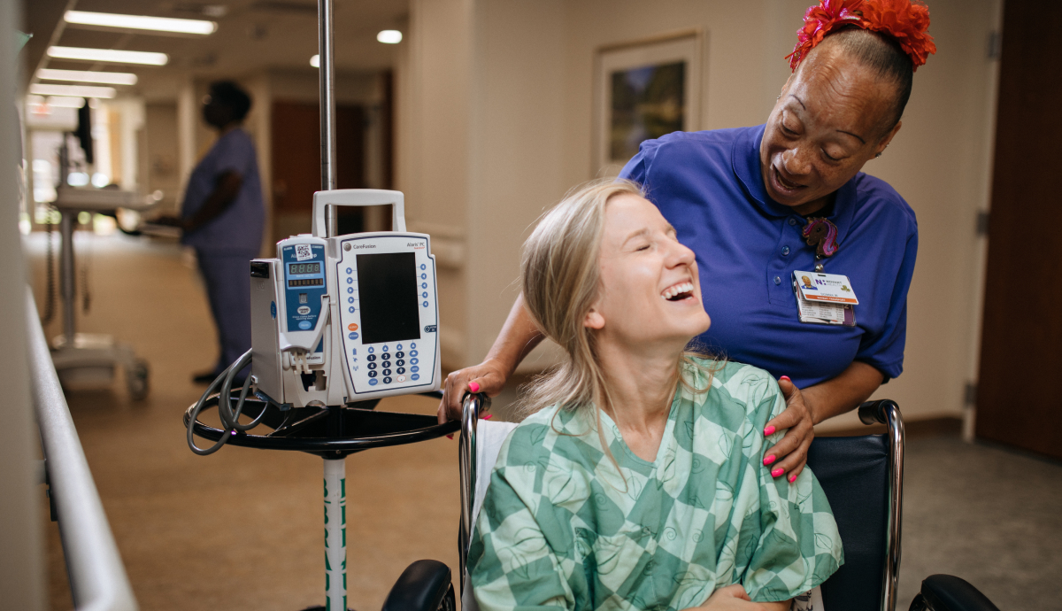 Nurse and patient smiling while using hospital equipment in a healthcare facility hallway.