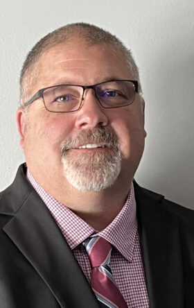 Middle-aged businessman with glasses, beard and checkered shirt and red tie smiling at camera