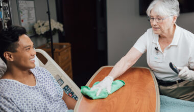 Friendly caregiver cleaning patient's hand in healthcare setting, providing attentive bedside care.