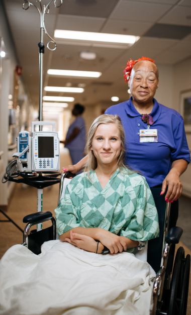 Patient smiling while nurse attends to medical equipment in hospital hallway