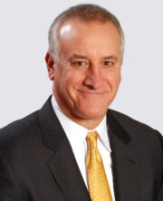Smiling businessman with short gray hair wearing black suit and yellow tie on white background