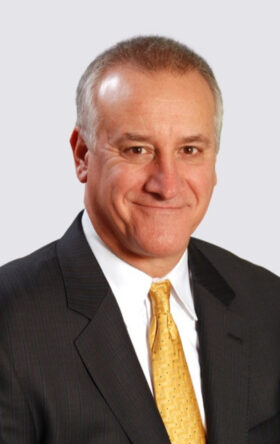 Smiling businessman with short gray hair wearing black suit and yellow tie on white background