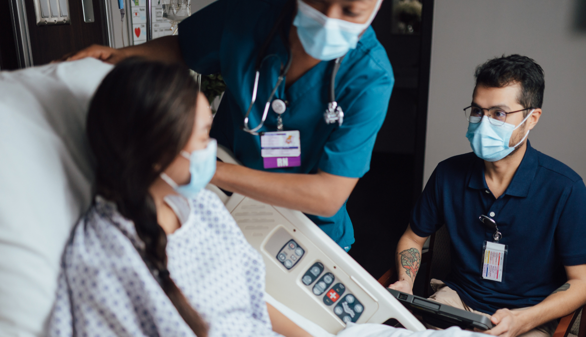Medical professionals wearing masks consult with patient in hospital room