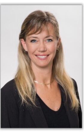 Smiling blonde woman in black shirt, professional headshot for healthcare services company website