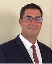 Smiling businessman wearing glasses and blue suit with red tie against light background, portrait photo