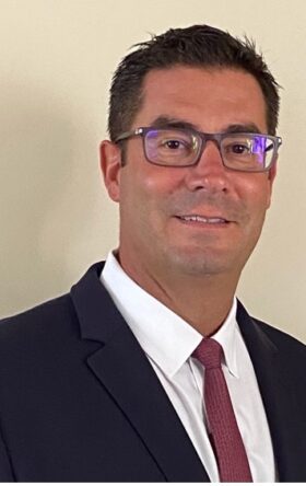 Smiling businessman wearing glasses and blue suit with red tie against light background, portrait photo