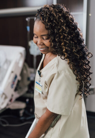 Smiling healthcare worker with curly hair and badge looking down in medical setting
