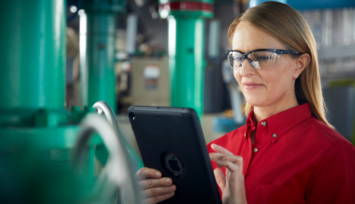 Blonde woman with glasses using tablet in industrial setting with green machinery in background