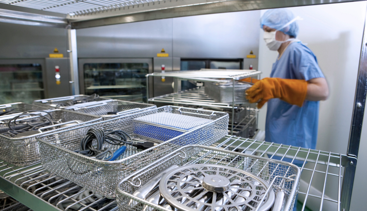 Metal surgical instrument trays being sanitized by a technician wearing protective gear