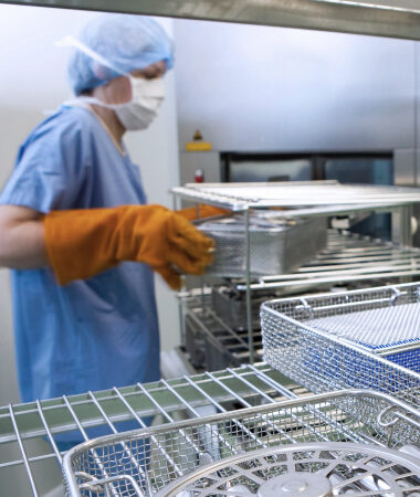 Technician inspecting surgical instruments on sterilization rack in hospital central sterile supply department