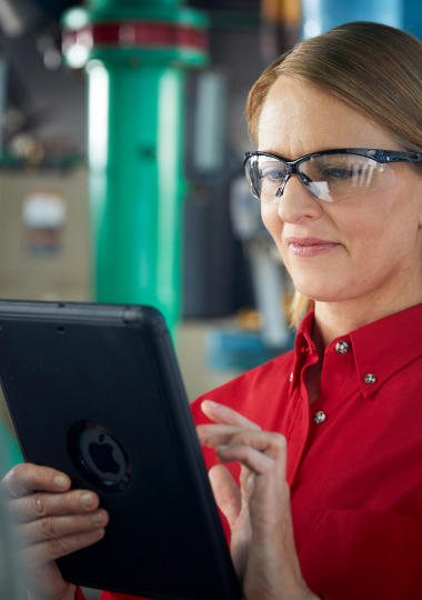Technician in red shirt and protective glasses using digital tablet for equipment maintenance