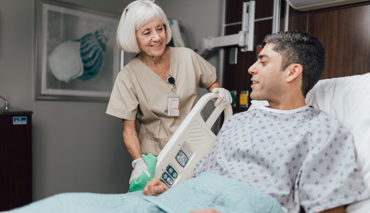 Elderly patient smiles while conversing with healthcare worker in hospital room