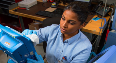 Alt text: Technician in blue shirt and gloves working with medical equipment in a laboratory setting.