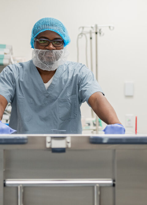 Alt text: Healthcare worker in protective gear and blue cap organizing medical supplies on metal shelves