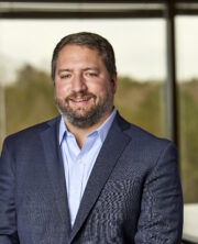 Middle-aged bearded businessman in suit smiling warmly in blurred office background
