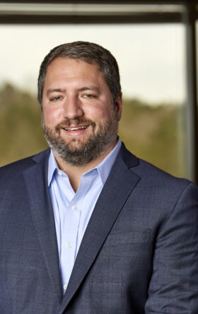 Middle-aged bearded businessman in suit smiling warmly in blurred office background