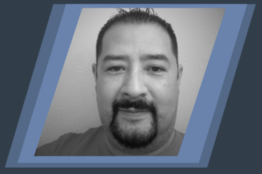 Alt text: Headshot photo of smiling middle-aged man with mustache and goatee against neutral background