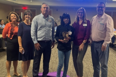 Group of smiling Crothall Healthcare employees pose together while holding award at company event