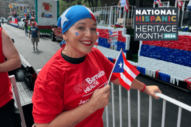 Woman in red shirt and blue headscarf smiles while holding small Puerto Rican flag at Hispanic Heritage Month event